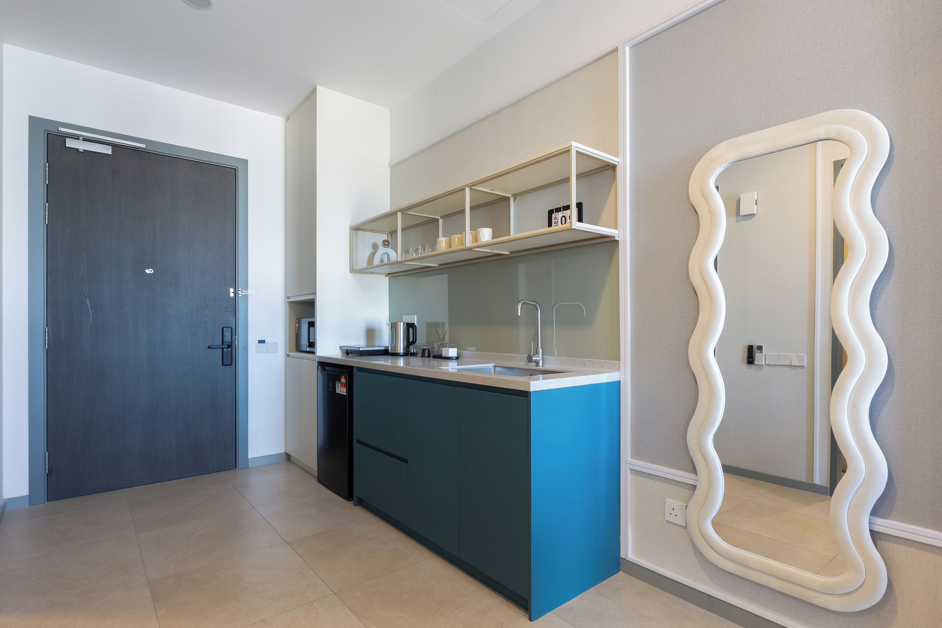 Una cocina moderna con una isla azul, estanterías blancas y un espejo ondulado único.