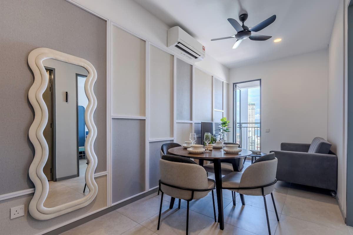 A modern living room with a dining area, a gray sofa, a unique wavy mirror, and a ceiling fan.
