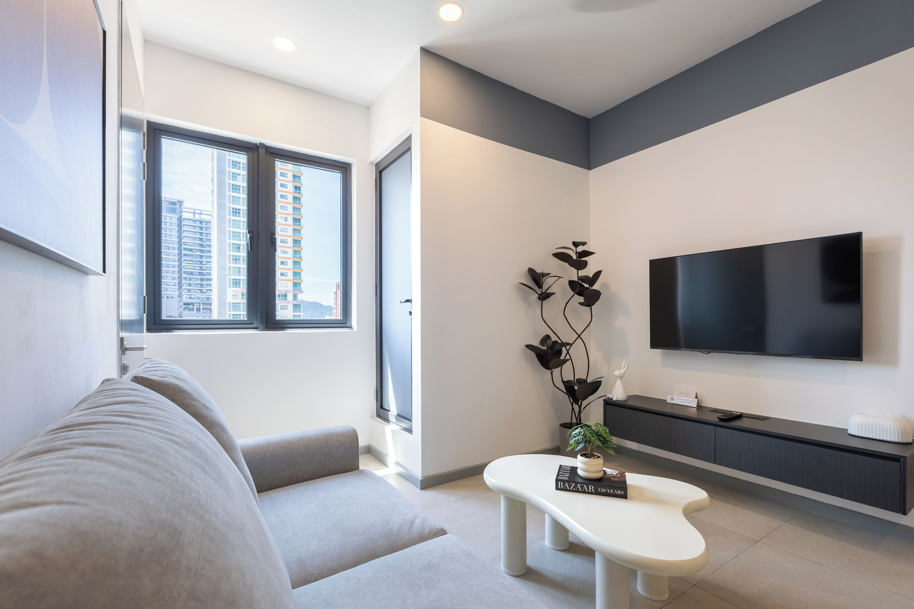 Een moderne woonkamer met een bank, salontafel, televisie en een plant.