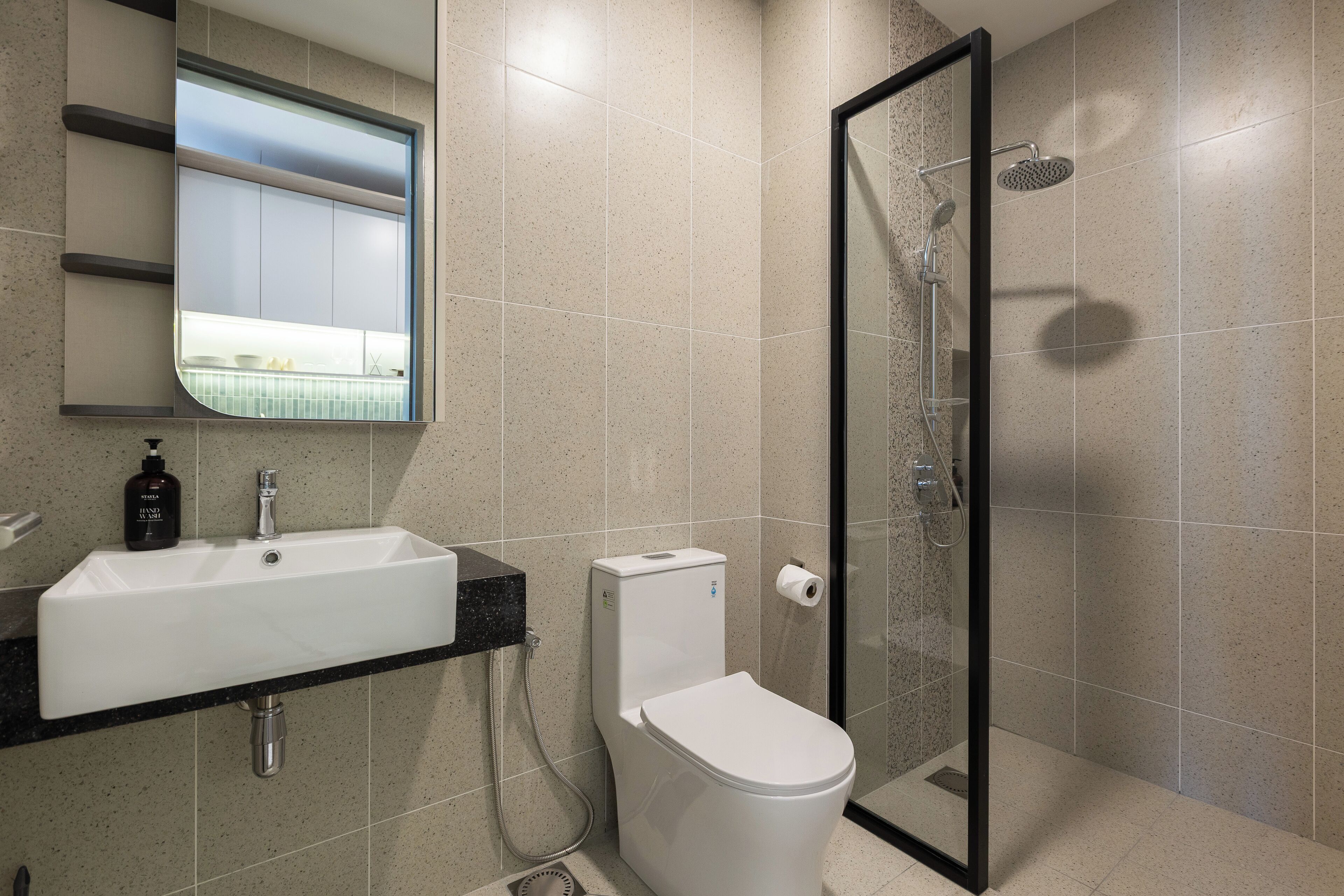 Un baño moderno con lavabo blanco, inodoro y ducha con mampara de vidrio.