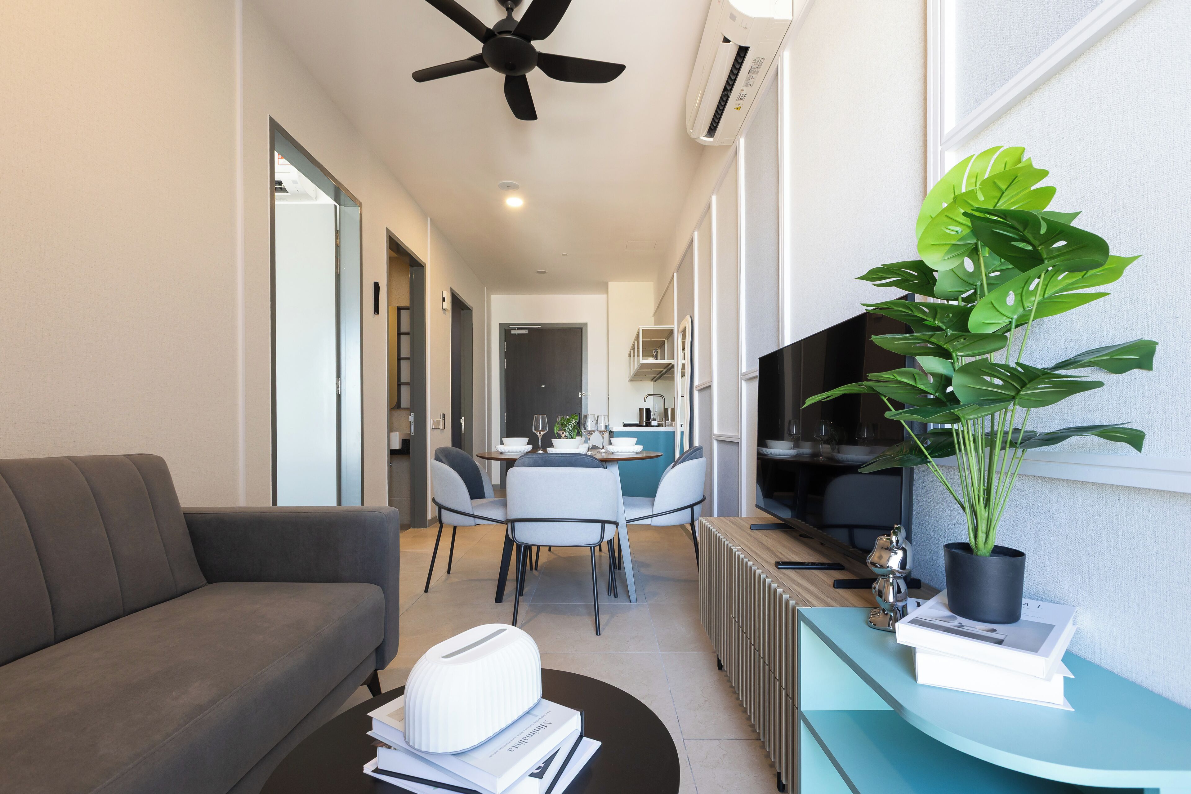 A modern living room with a sofa, dining table, chairs, a ceiling fan, and a potted plant.