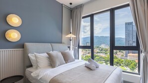 A modern hotel room with a large bed, a bedside table, and a view of the city through large windows. - 22 Macalisterz (George Town)