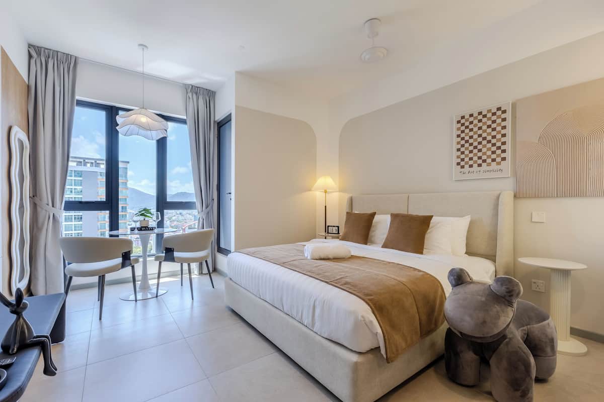 A modern hotel room with a large bed, a desk with chairs, a view of the city, and a decorative wall piece.
