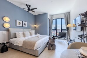Ein modernes Hotelzimmer mit einem großen Bett, einem Deckenventilator, Blick auf die Stadt und einer Essecke mit Tisch für zwei Personen.