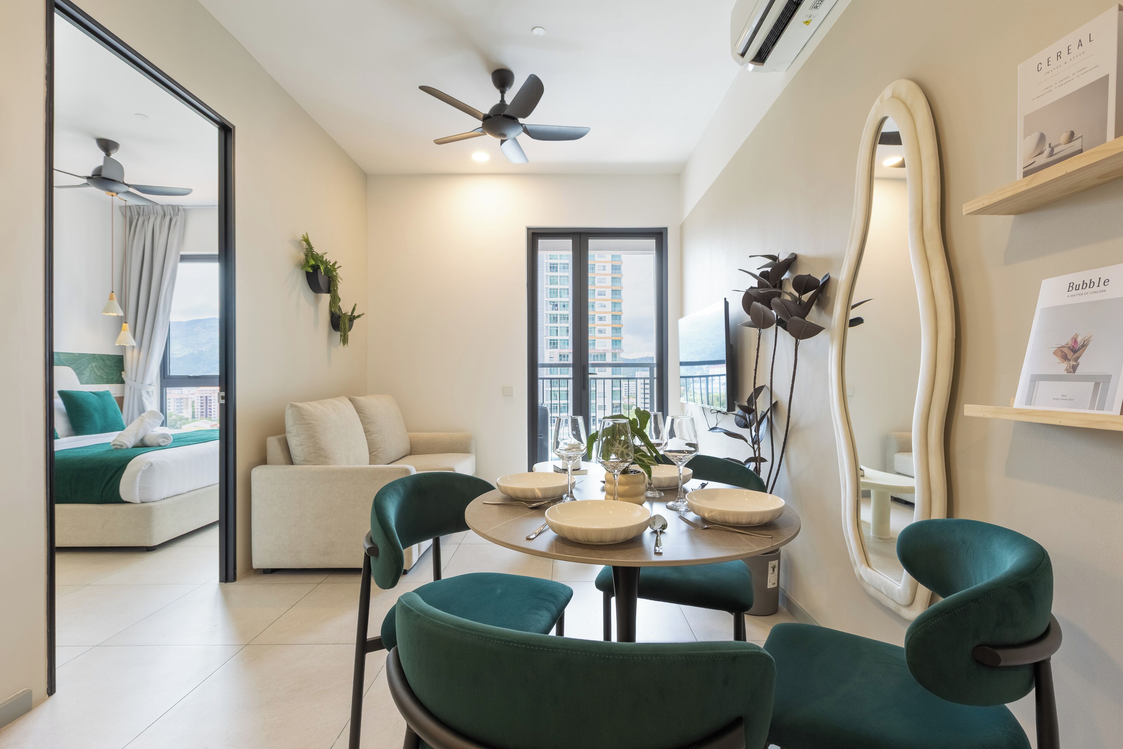 A modern dining area with a round table, green chairs, and a large mirror on the wall.