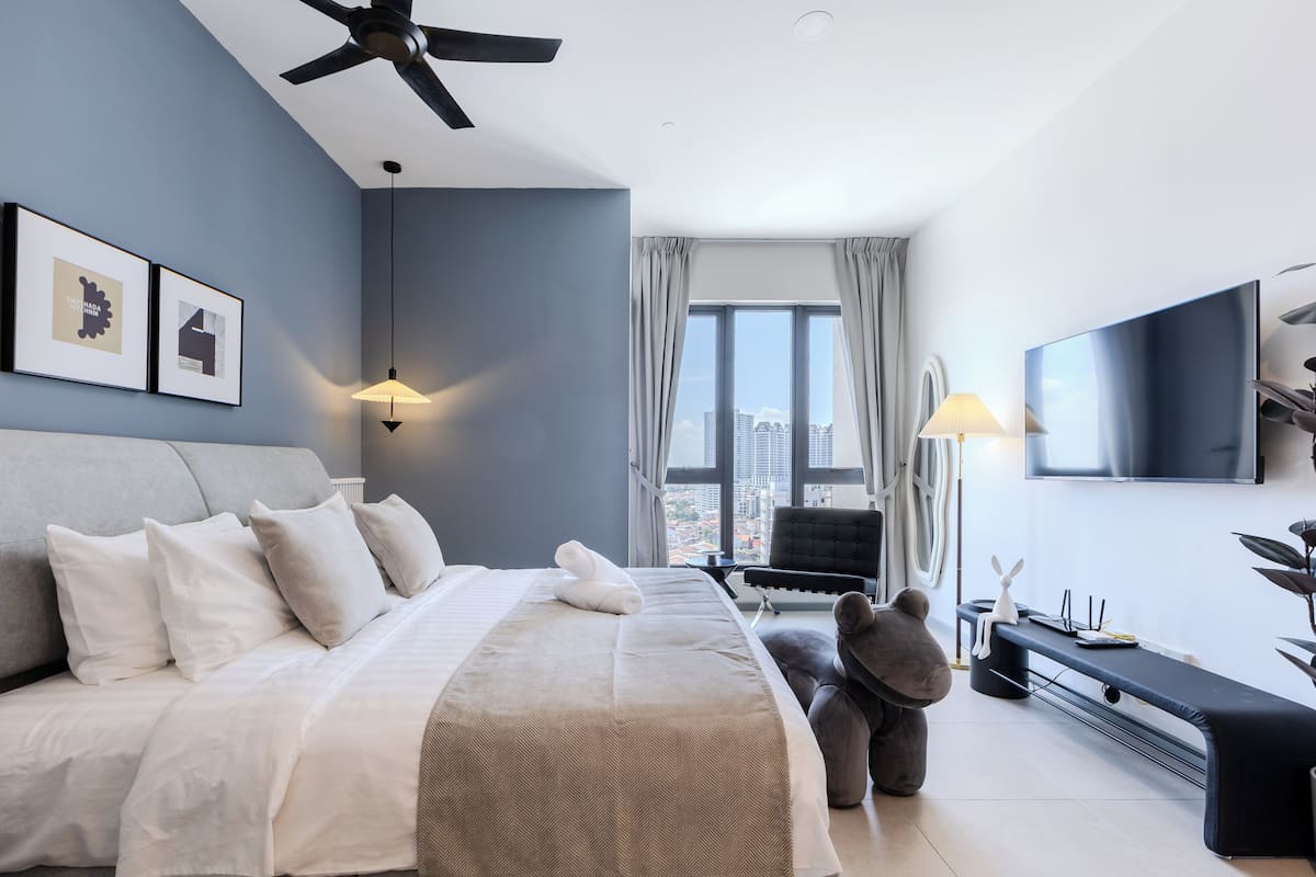 A modern hotel room with a large bed, a ceiling fan, a flat-screen TV, and a city view.