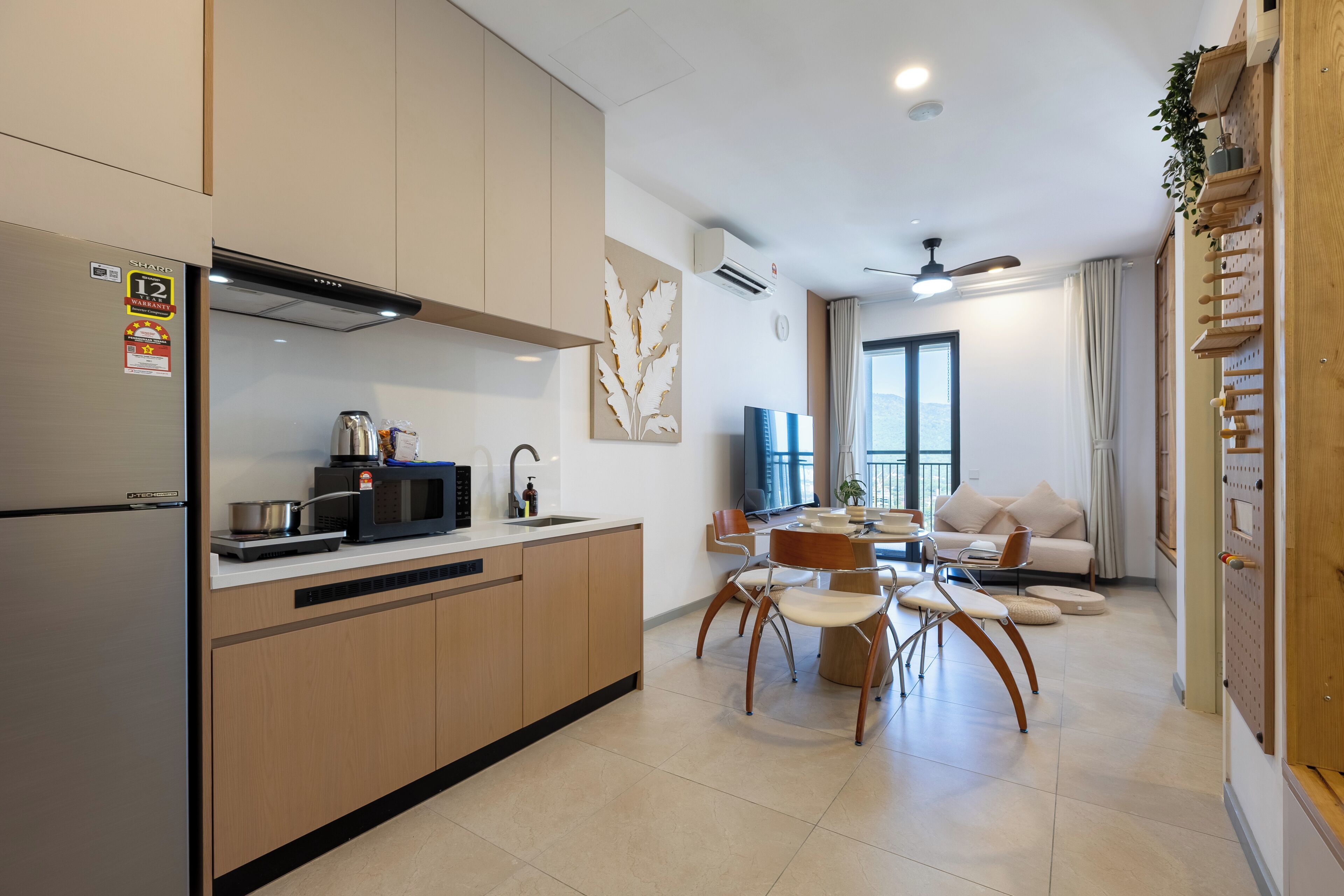 A modern kitchen with a refrigerator, microwave, and stove, a dining area with chairs and a table, and a living room with a sofa and a TV.