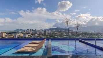 A rooftop infinity pool with a cityscape view, including mountains and a city skyline.