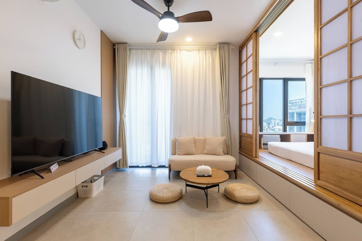 A modern living room with a flat-screen TV, a sofa, a round coffee table, and a view of the city through large windows.
