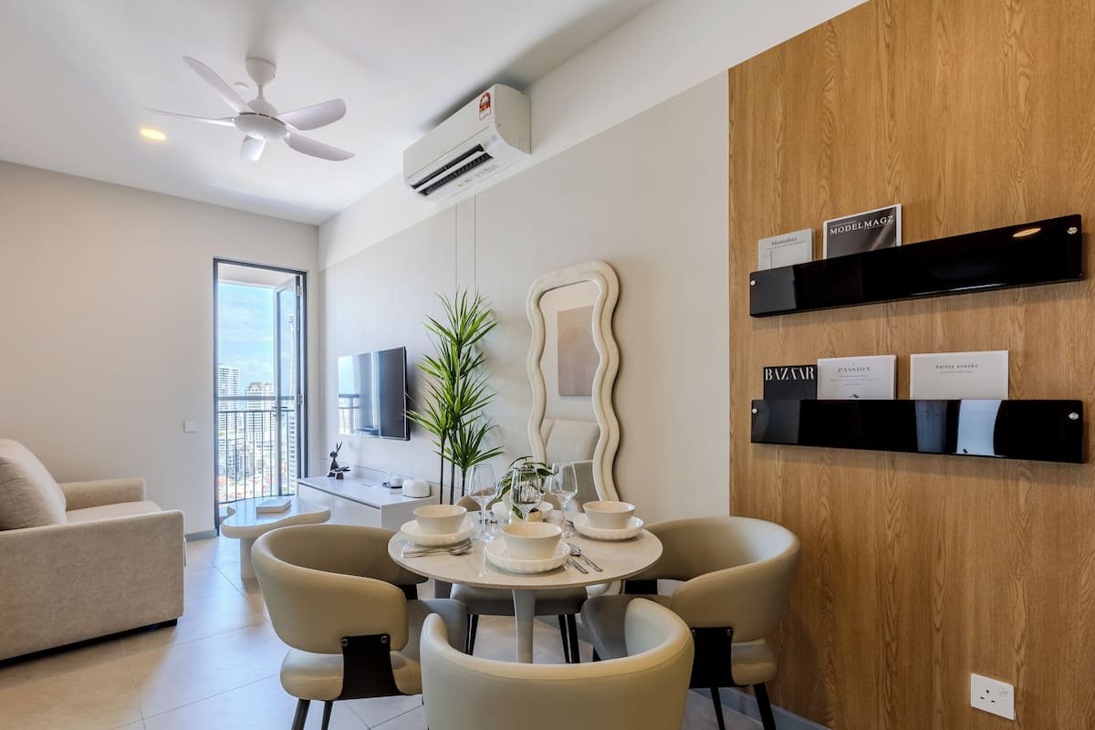 A modern living room with a dining area, a ceiling fan, an air conditioning unit, a large mirror, and a wooden wall with magazine holders.