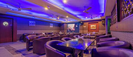 A room with multiple seating areas, ceiling fans, and a television screen.