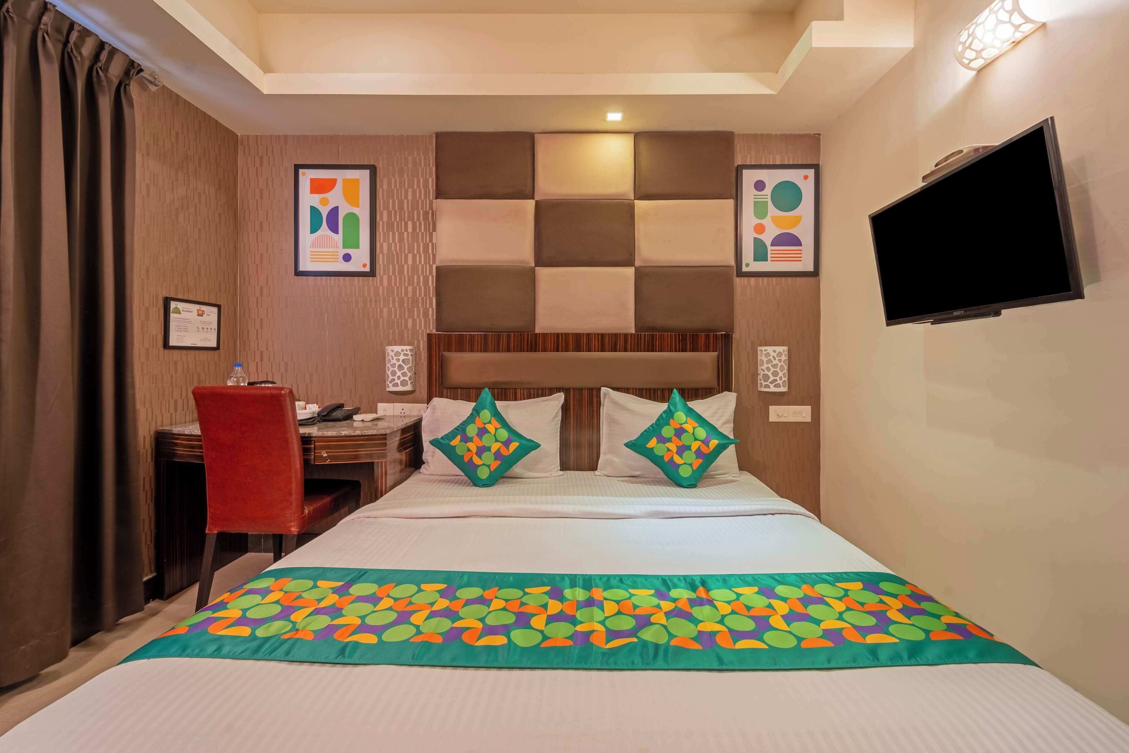 A hotel room with a bed, a desk, a chair, a television, and artwork on the walls.