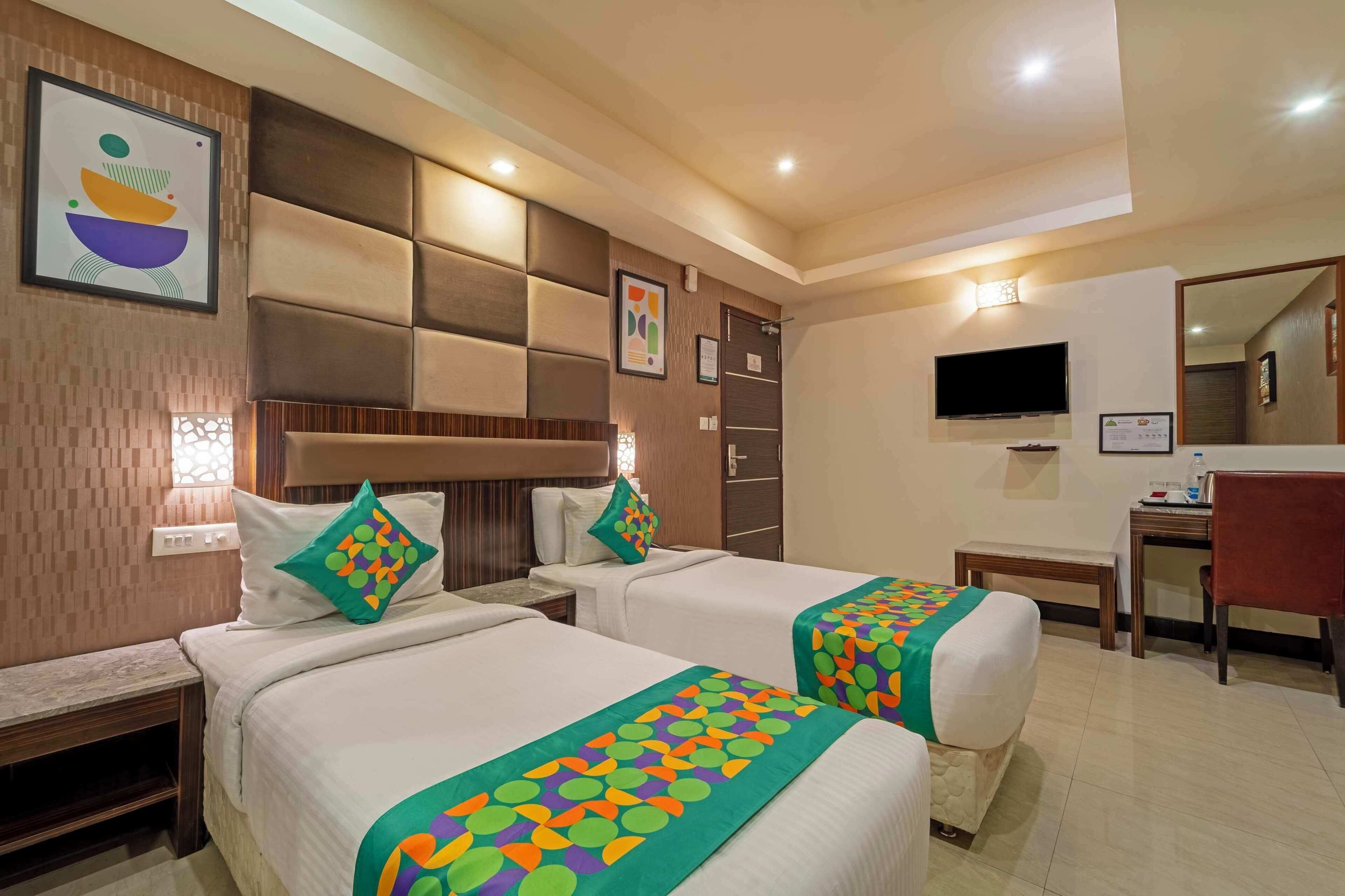 A hotel room with two beds, a desk, a chair, and a TV.