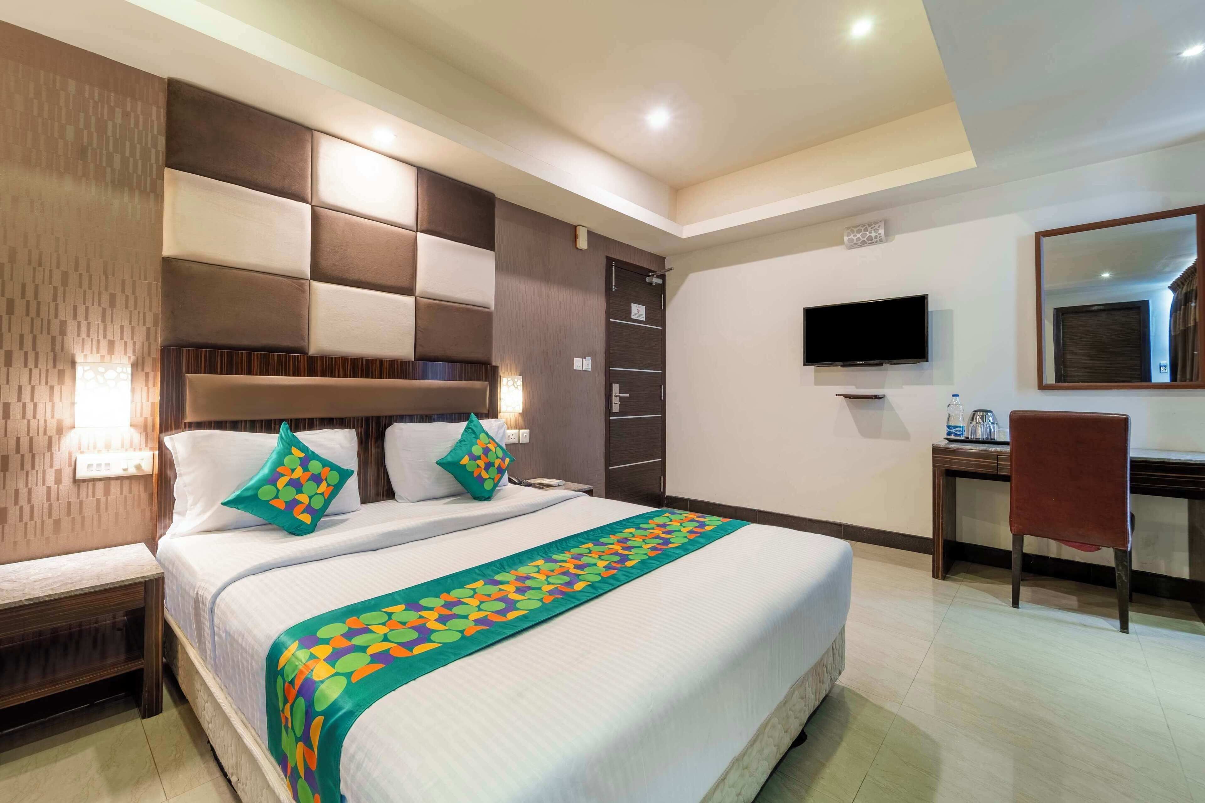 A hotel room with a large bed, a desk, a chair, a TV, and a wardrobe.