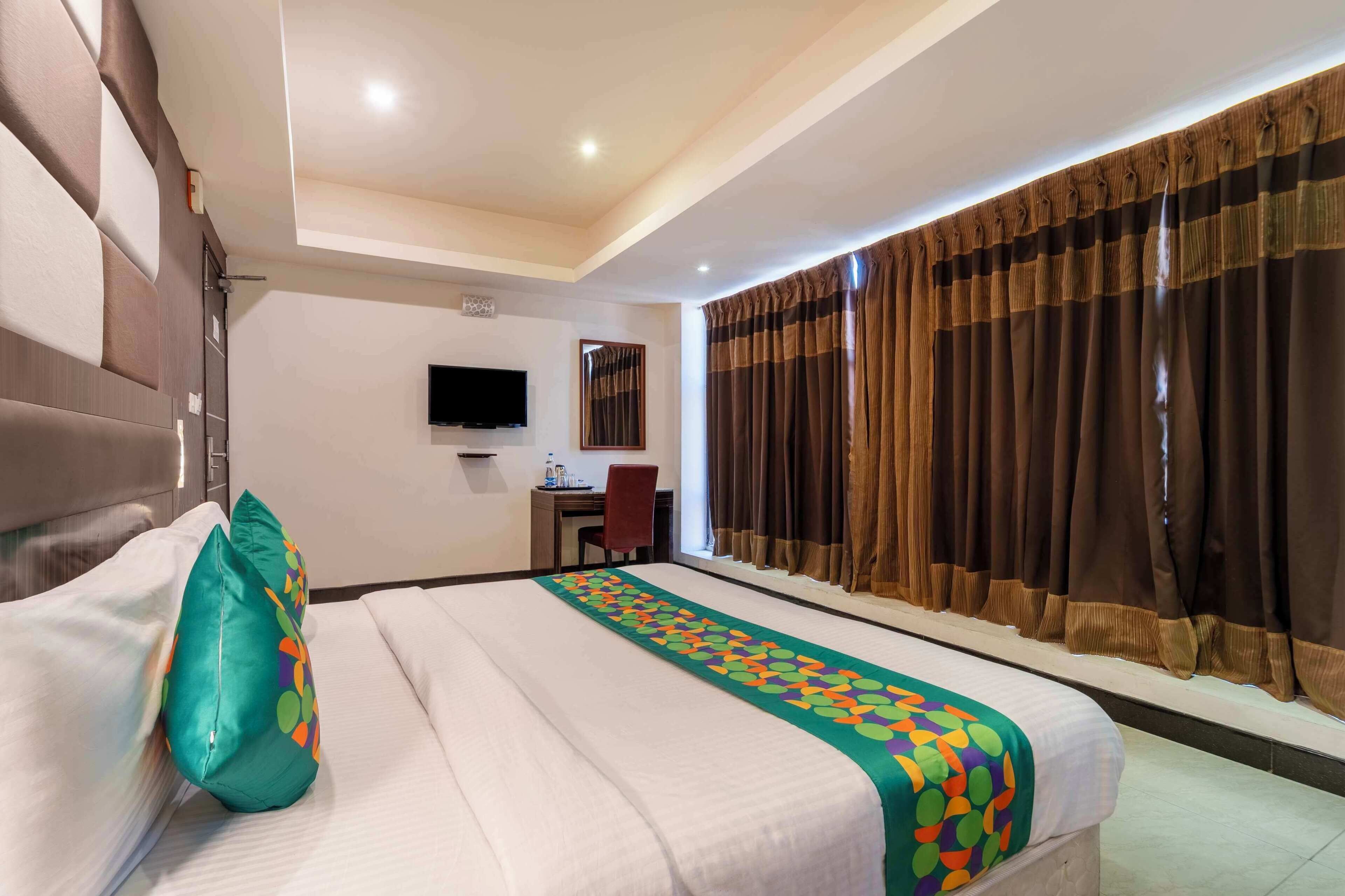 A hotel room with a bed, a desk, a chair, a television, and curtains.