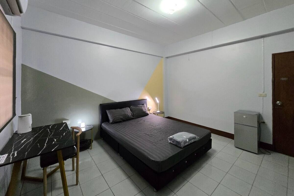 Een slaapkamer met een bed, een bureau, een stoel, een nachtkastje, een lamp en een klein kastje.