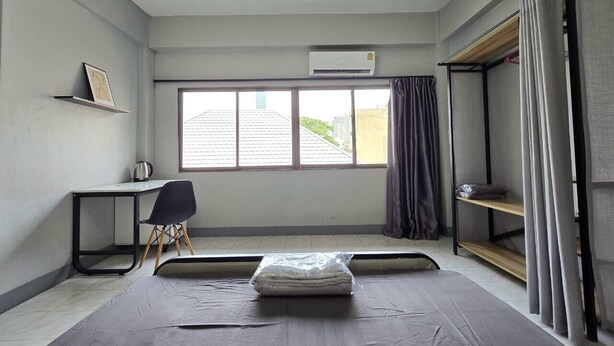 Een kleine kamer met een bed, bureau, stoel en een raam met gordijnen.