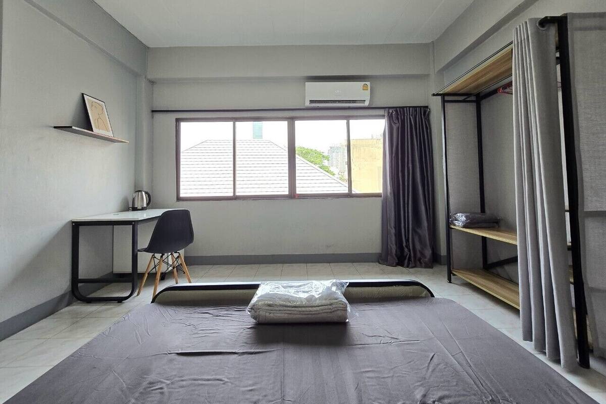 Een kleine kamer met een bed, bureau, stoel en een raam met gordijnen.