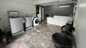 Een compact woongedeelte met een wasmachine, een kleine koelkast, een eethoek met tafel en stoelen, en een kitchenette met een spoelbak en aanrecht.