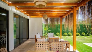 A covered outdoor seating area with wicker furniture and a table, a wooden pergola overhead, and a view of a well-maintained garden. - Jessic Villas (Hisarönü)