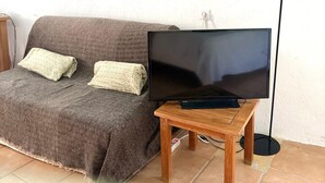 Uma sala de estar com um sofá, uma televisão de tela plana sobre um suporte de madeira e dois quadros pendurados na parede.