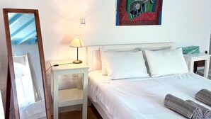 Quarto com cama, mesa de cabeceira, abajur, espelho e um quadro na parede.