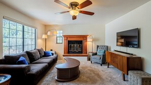 A living room with a fireplace, a ceiling fan, a television, and a large window. - Family and Pet Friendly Desert Haven in Central Tucson (Tucson)