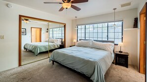 A bedroom with a large mirror, two beds, a ceiling fan, a window with blinds, and a nightstand with a lamp. - Family and Pet Friendly Desert Haven in Central Tucson (Tucson)