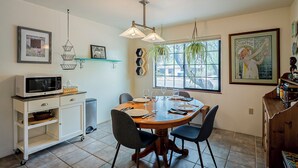 A dining area with a round wooden table, black chairs, a white cabinet with a microwave, and a hanging light fixture. - Family and Pet Friendly Desert Haven in Central Tucson (Tucson)