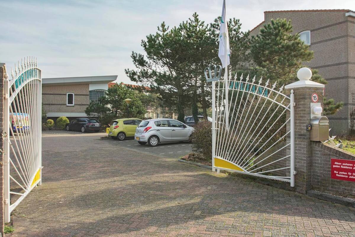 Een toegangspoort met een gebouw van baksteen, een bord met een snelheidslimiet van 15, en geparkeerde auto's.
