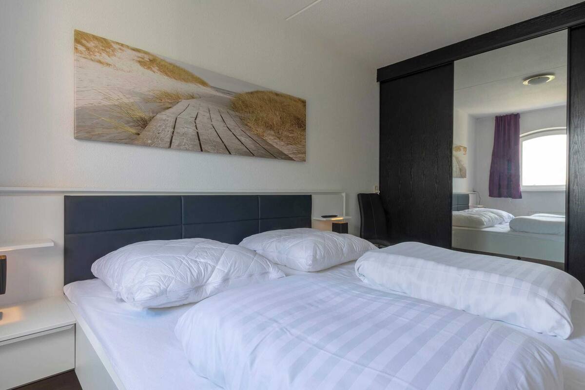 Een hotelkamer met een groot bed, een hoofdbord, een nachtkastje, een spiegel en een aan de muur hangend schilderij.