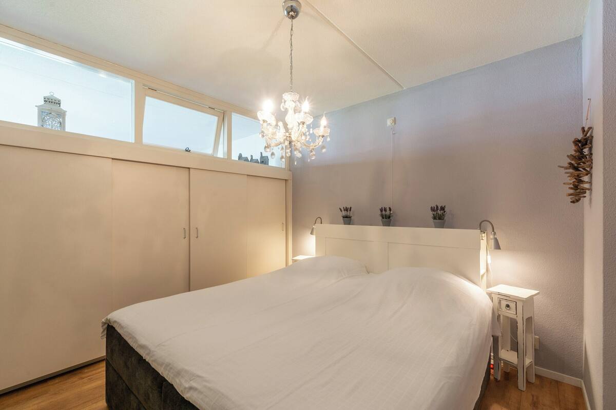 Een slaapkamer met een groot bed, een kroonluchter, een nachtkastje en een garderobe.