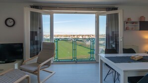 Una stanza con balcone, televisione, tavolo con asciugamano e orologio a parete.