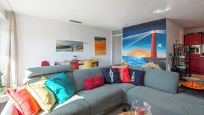 Ein modernes Wohnzimmer mit einem grauen Sofa, bunten Kissen, einem Gemälde eines Leuchtturms und einem roten Schrank.