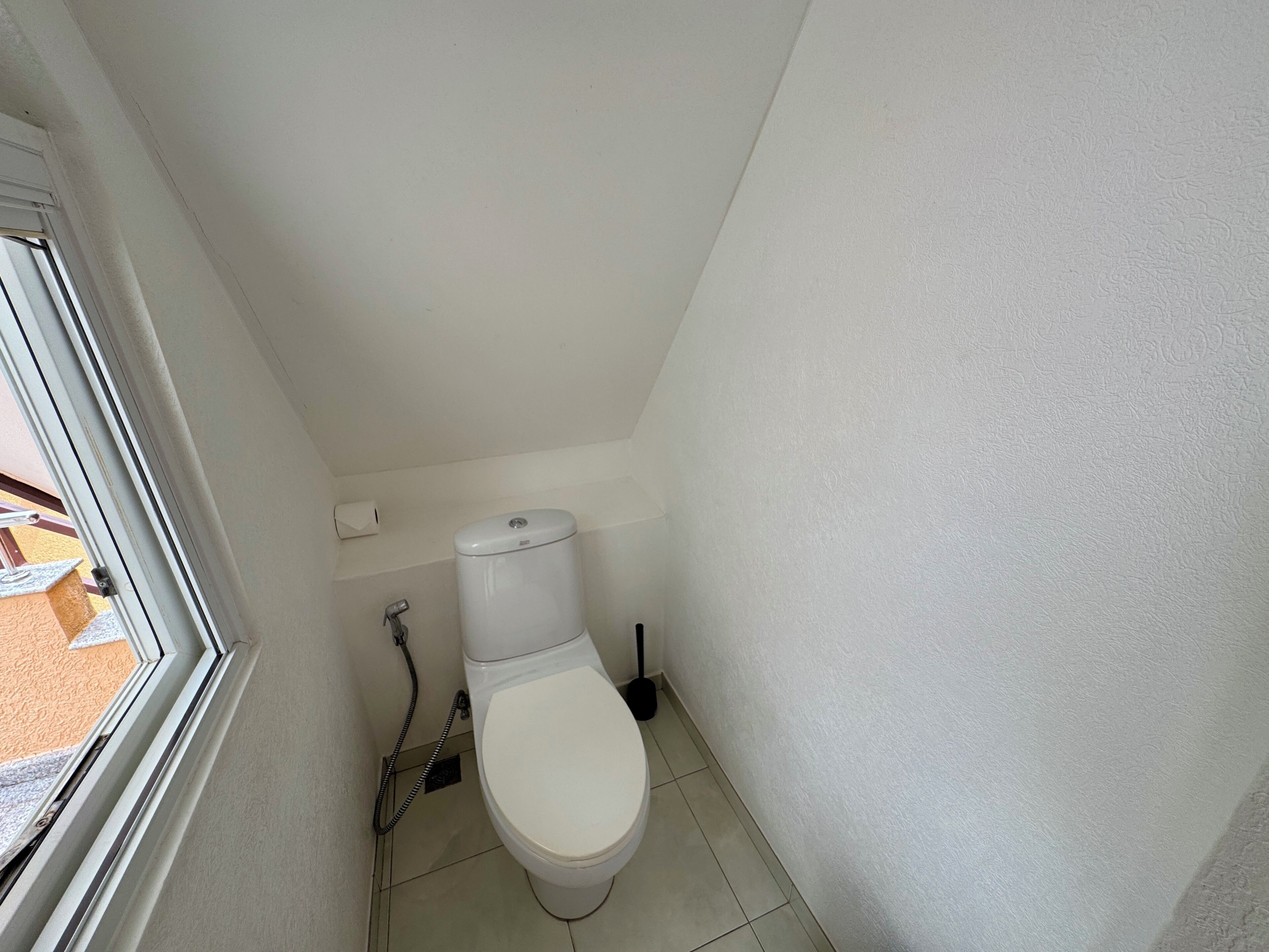 Un baño pequeño y estrecho con inodoro, porta rollos y un desatascador.