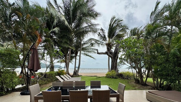 Eine Terrasse mit Tisch und Stühlen mit Blick auf einen Strand mit Palmen.