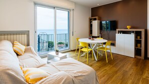 A modern bedroom with a large bed, a balcony with a view, a dining area with yellow chairs, and a TV on the wall. - Ginestra by Interhome (Alassio)