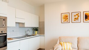 A modern kitchen with white cabinets, a built-in oven, and a sink. There is a dining table with a plant and a vase. A sofa with yellow pillows is in the living area. - Ginestra by Interhome (Alassio)