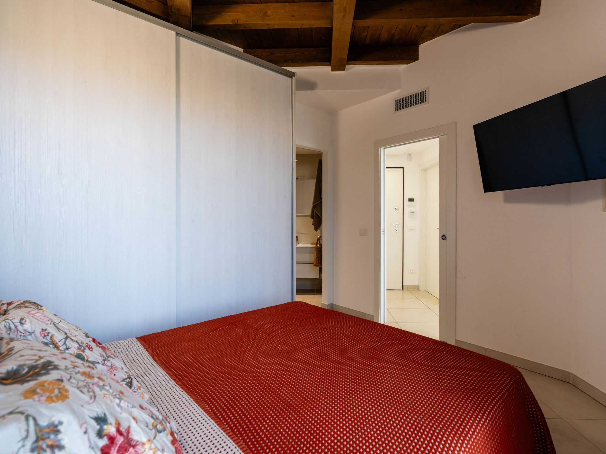 A bedroom with a bed, a wardrobe, a television, and a staircase leading to another room.