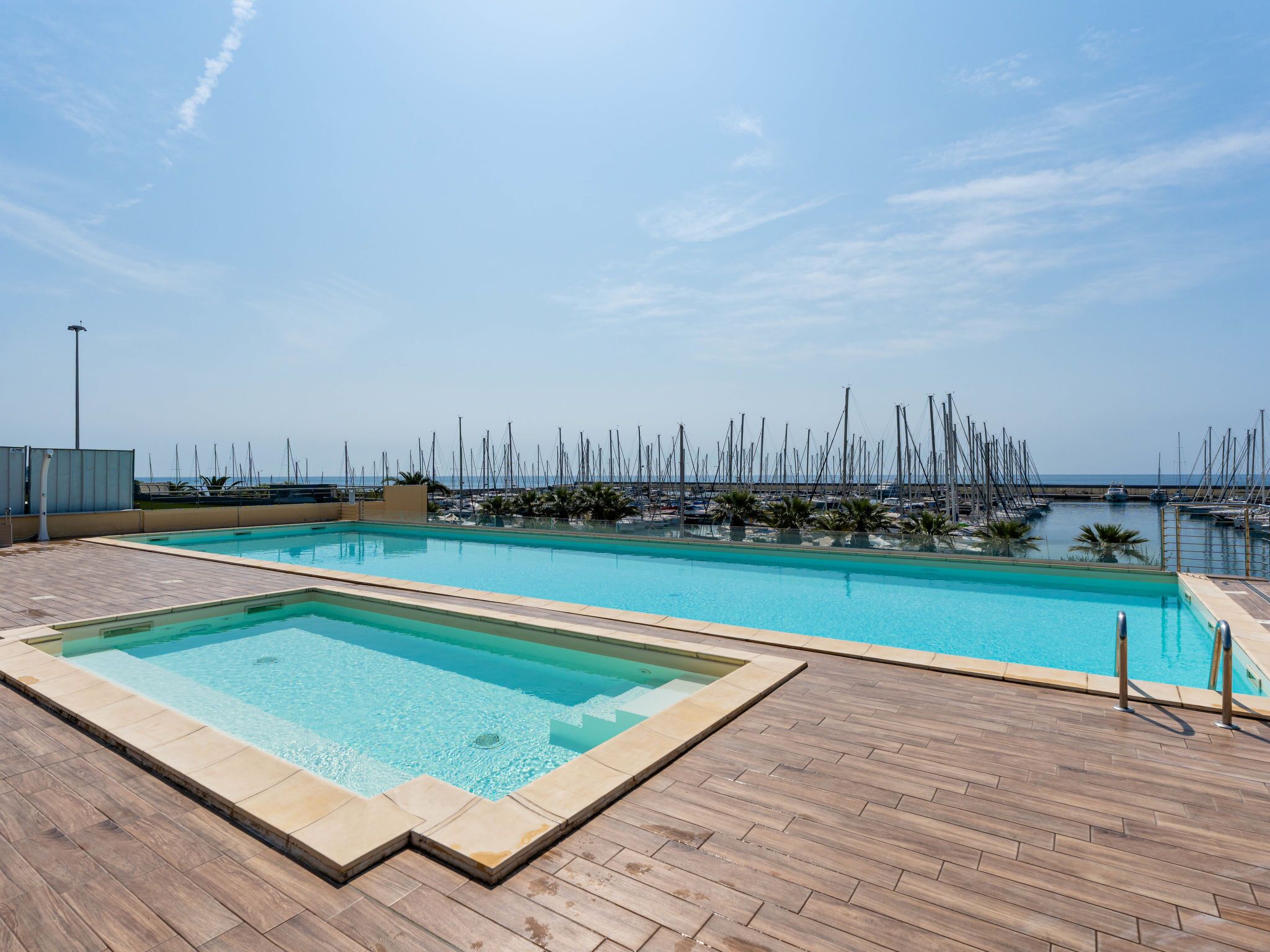 Una piscina con muelle de madera, rodeada por un puerto deportivo con numerosos barcos.