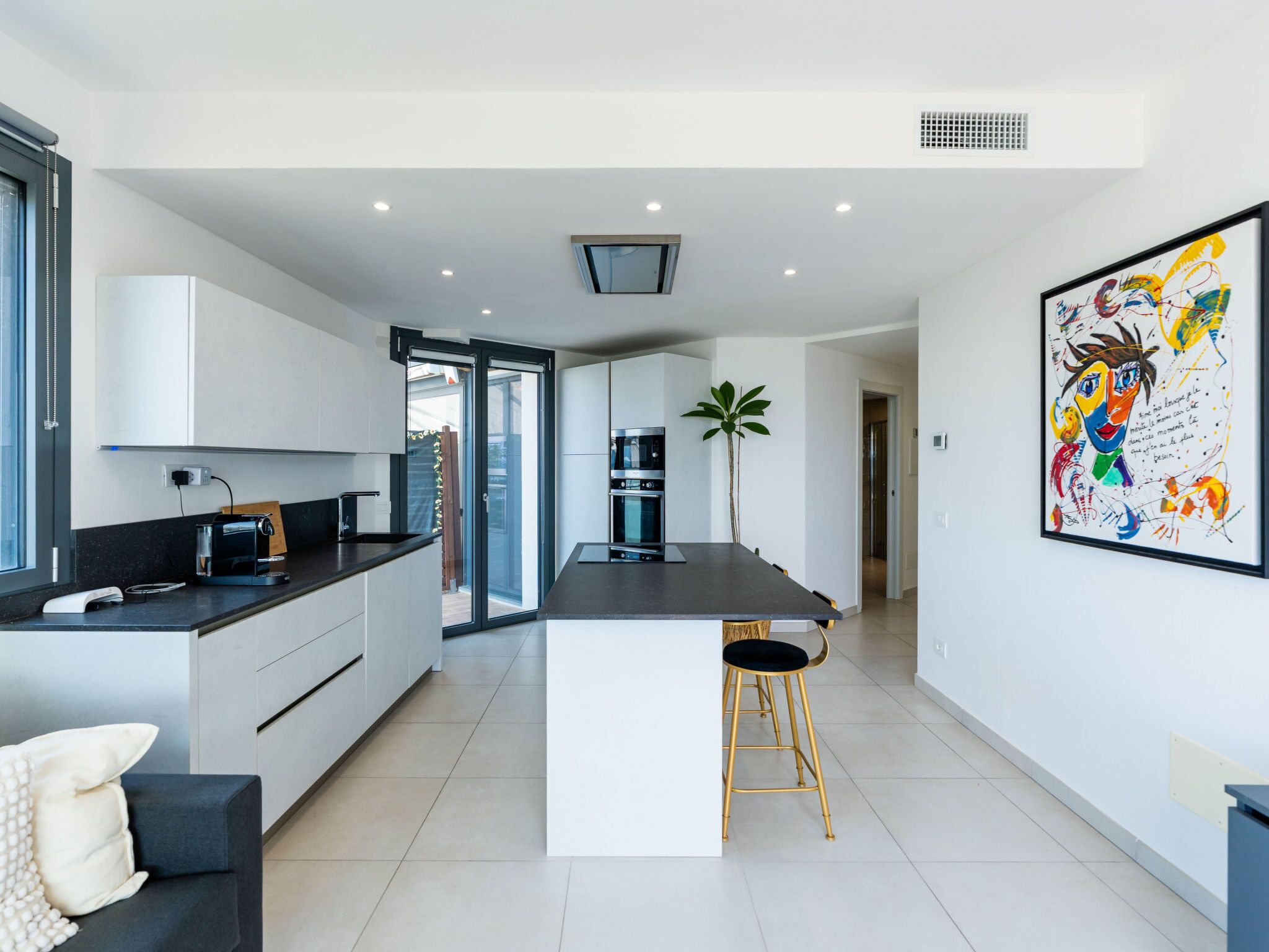 Une cuisine moderne avec un îlot central, un coin repas doté d’un canapé noir et un grand tableau abstrait accroché au mur.