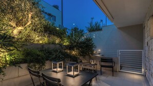 En udendørs terrasse med borde og stole, omgivet af planter og en mur.