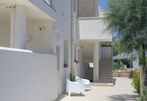 A modern building with a clean, minimalist design, featuring a staircase leading to an upper level, outdoor seating area, and a well-maintained garden. - Ginepro - Shelter by the sea in Apulia | A few steps from the beach (Puglia)