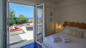 A hotel room with a bed, a nightstand, a wall-mounted lamp, and a view of an outdoor seating area with a table and chairs. - Ginepro - Shelter by the sea in Apulia | A few steps from the beach (Puglia)