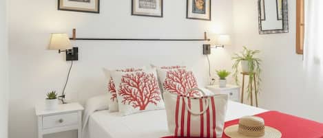 A neatly arranged hotel room with a bed, two bedside tables, a red throw blanket, and wall-mounted lamps.