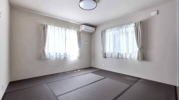 A room with tatami mats, two windows with curtains, an air conditioning unit, and a ceiling light.