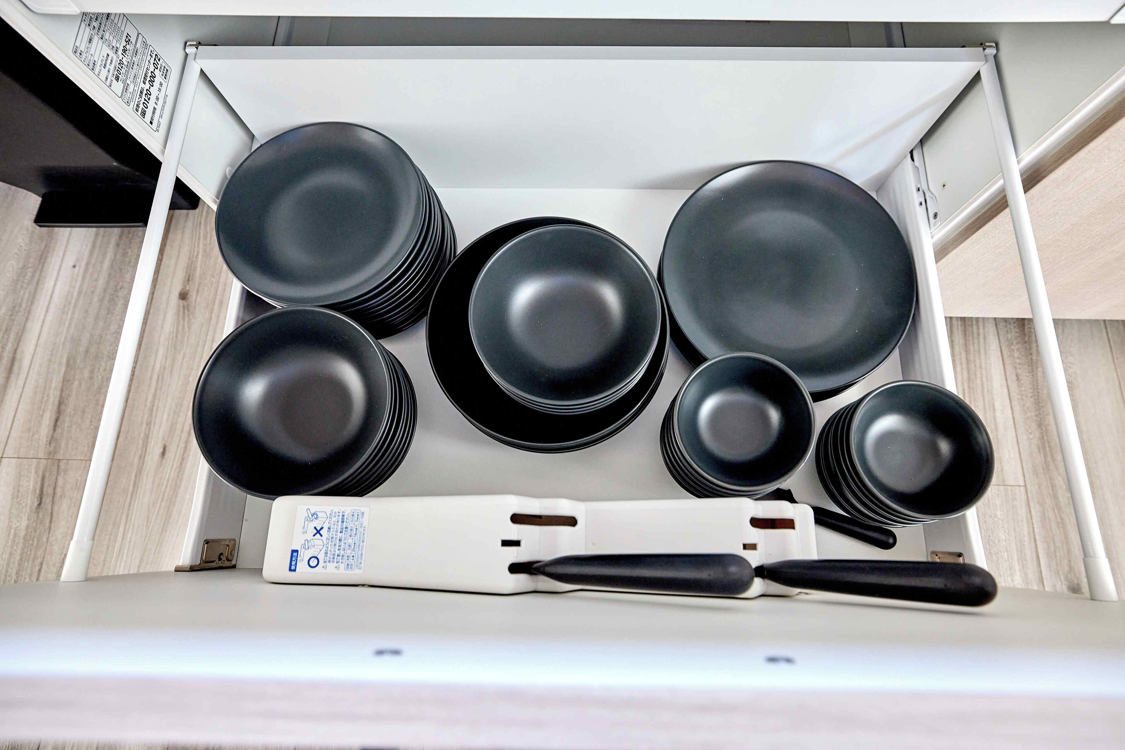 A drawer containing black plates and a white utensil with a black handle.