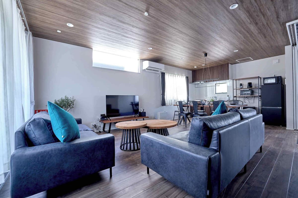 Een moderne woonkamer met een bank, salontafel en televisie. Er is een keukenhoek met een koelkast en magnetron.