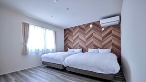 Een hotelkamer met twee bedden, een houten visgraat wand en een groot raam met gordijnen.
