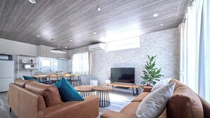 Een moderne woonkamer met een bruine leren bank, een televisie, en een eethoek met een houten tafel en stoelen.